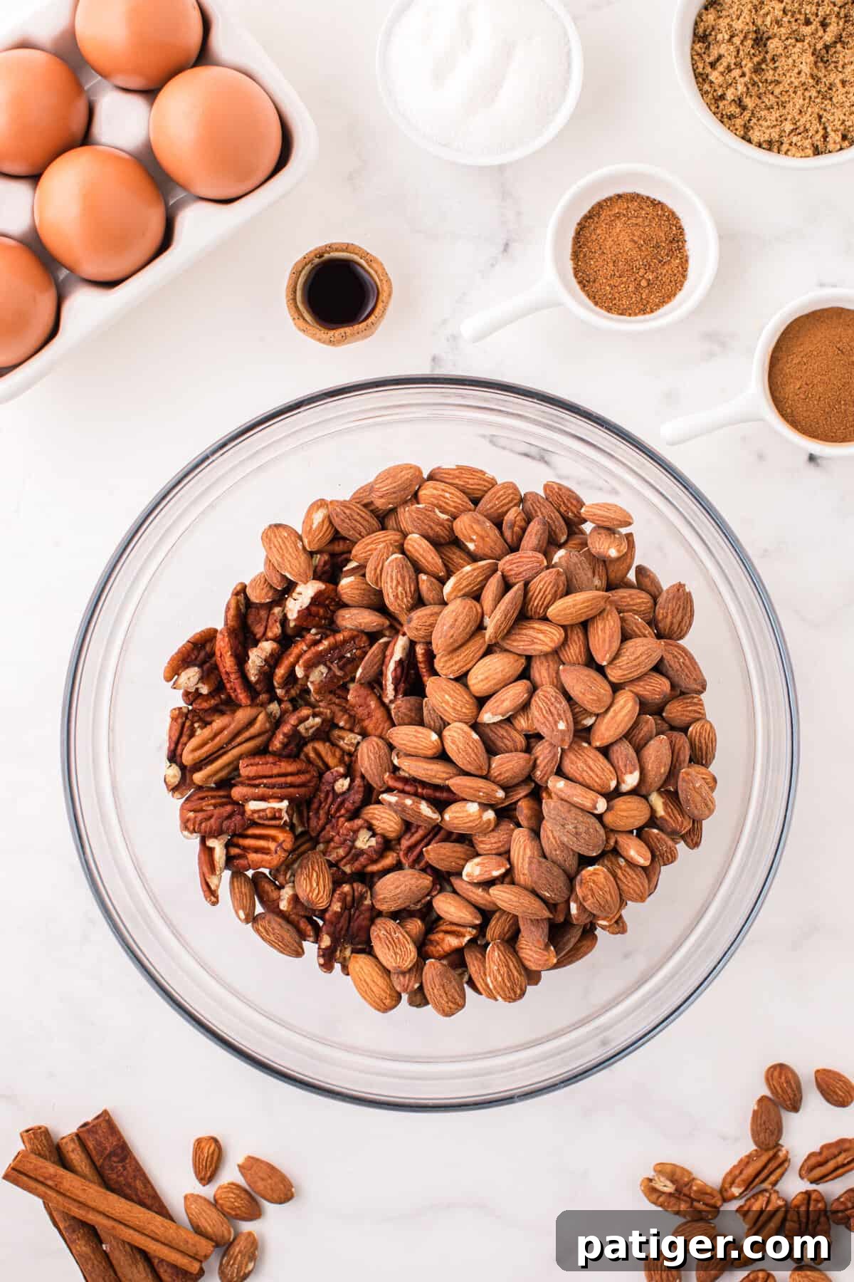 Raw almonds and pecan halves in a glass mixing bowl, ready for coating.