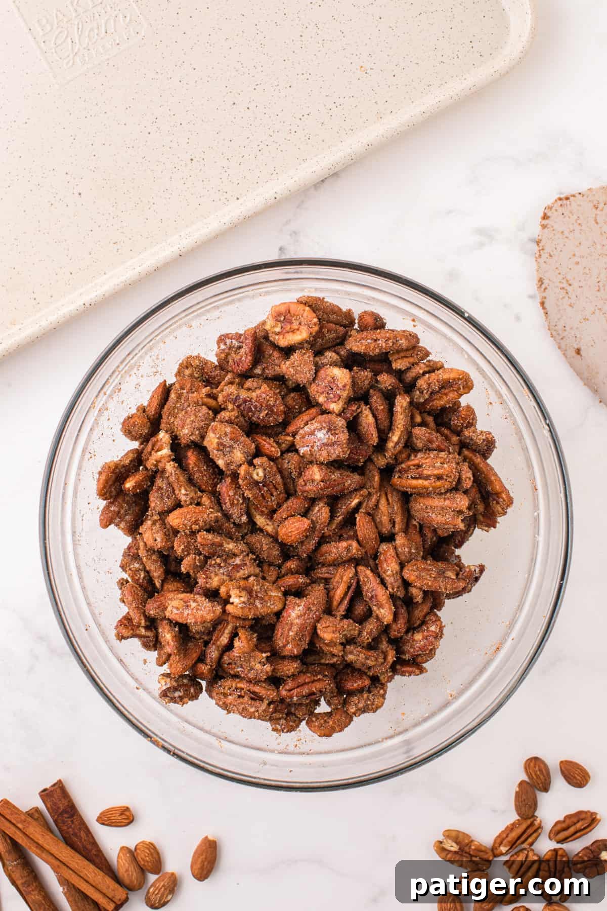 Almonds and pecans coated in the sugar and spice mixture in a mixing bowl.