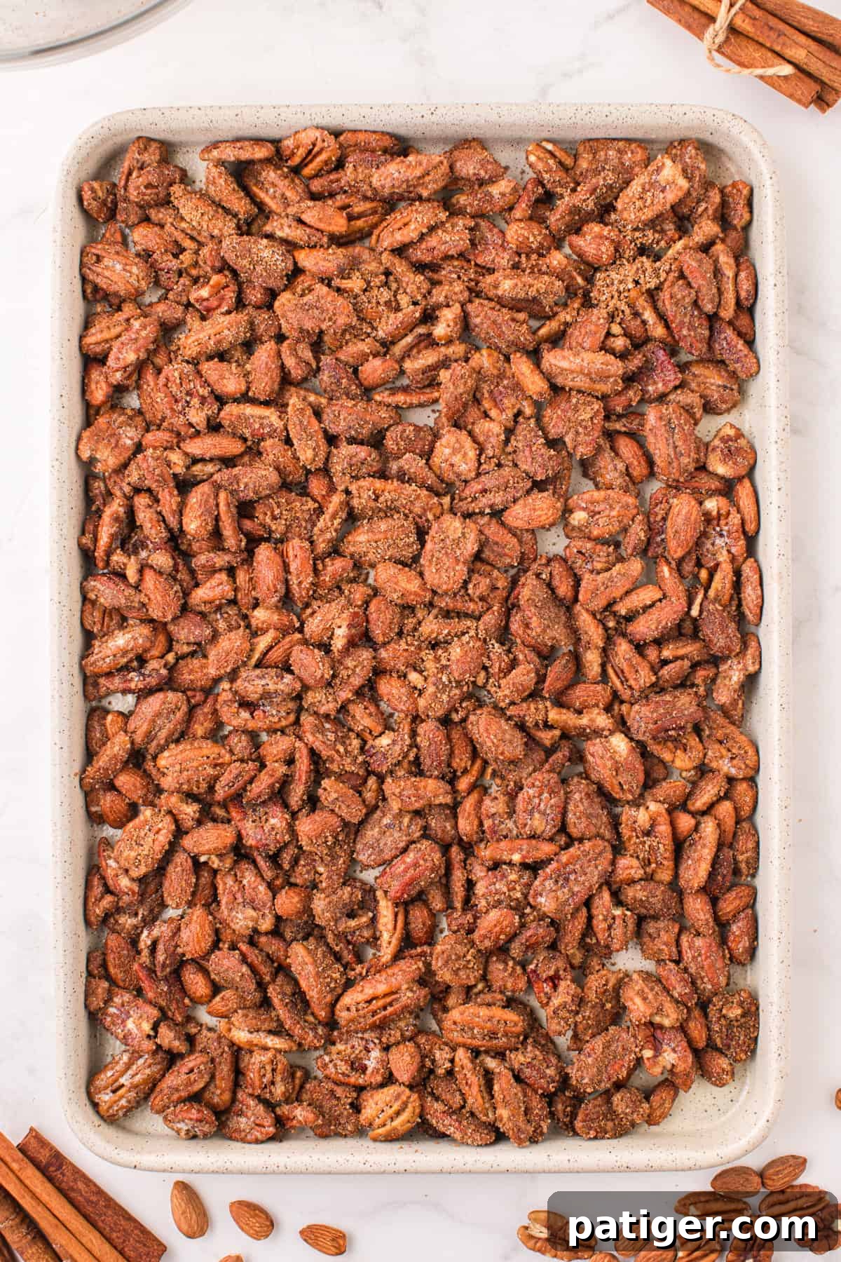 Coated nuts spread in an even layer on a baking sheet, ready for the oven.