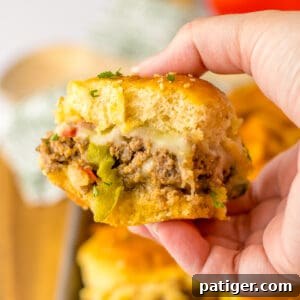 Hand holding a ground beef philly cheesesteak slider on a Hawaiian Roll with peppers and onions.