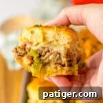 Hand holding a ground beef philly cheesesteak slider on a Hawaiian Roll with peppers and onions.