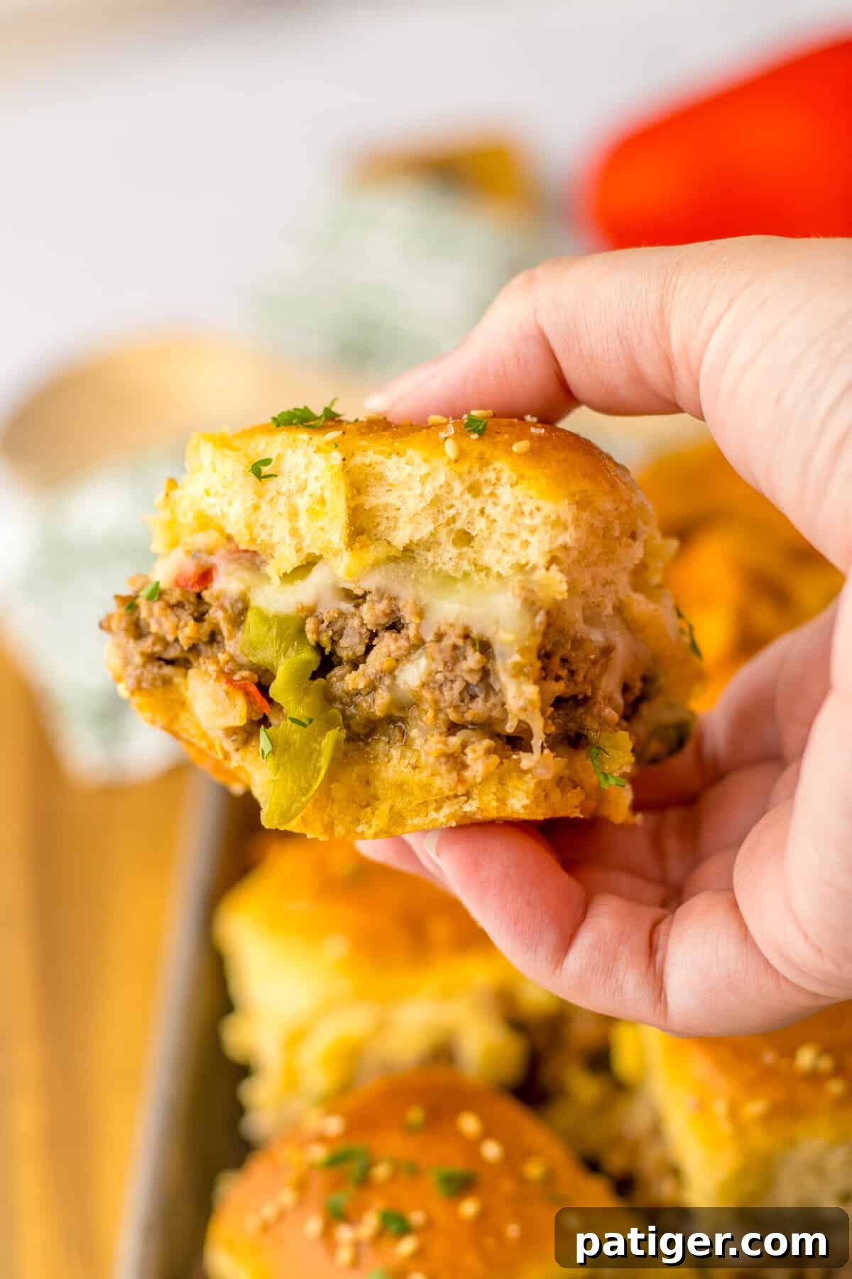 Gooey Philly Slider Perfection 3 A hand holding a ground beef Philly cheesesteak slider, showcasing the melted cheese, peppers, and onions.