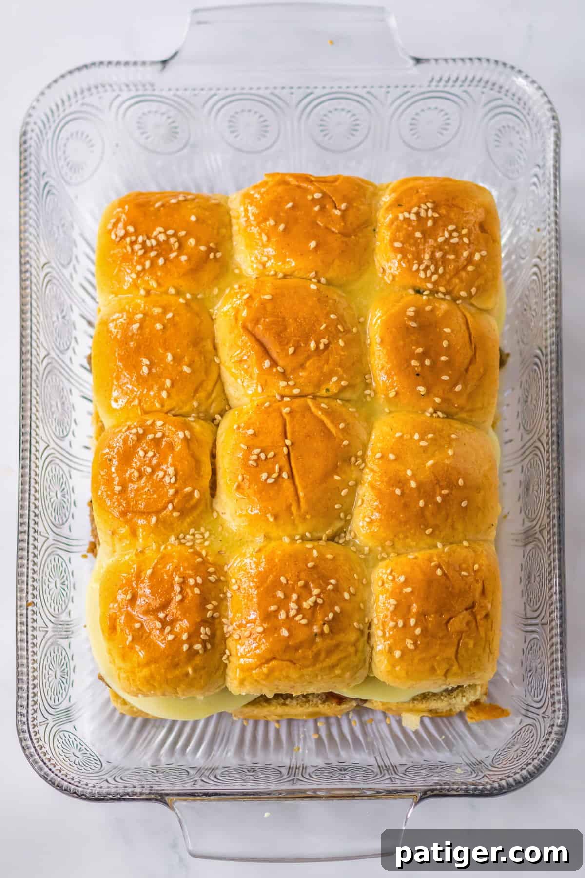 Gooey Philly Slider Perfection 8 Philly Cheesesteak Sliders assembled in a 9x13 casserole dish with buttered and sesame-seeded tops, ready for baking.