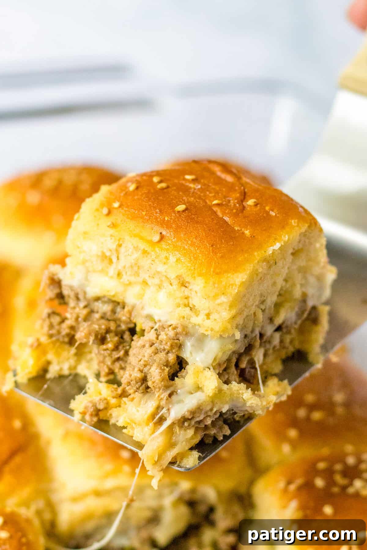 Gooey Philly Slider Perfection 9 A ground beef Philly cheesesteak slider being carefully lifted from the baking dish with a metal turner, showing the melted cheese and filling.