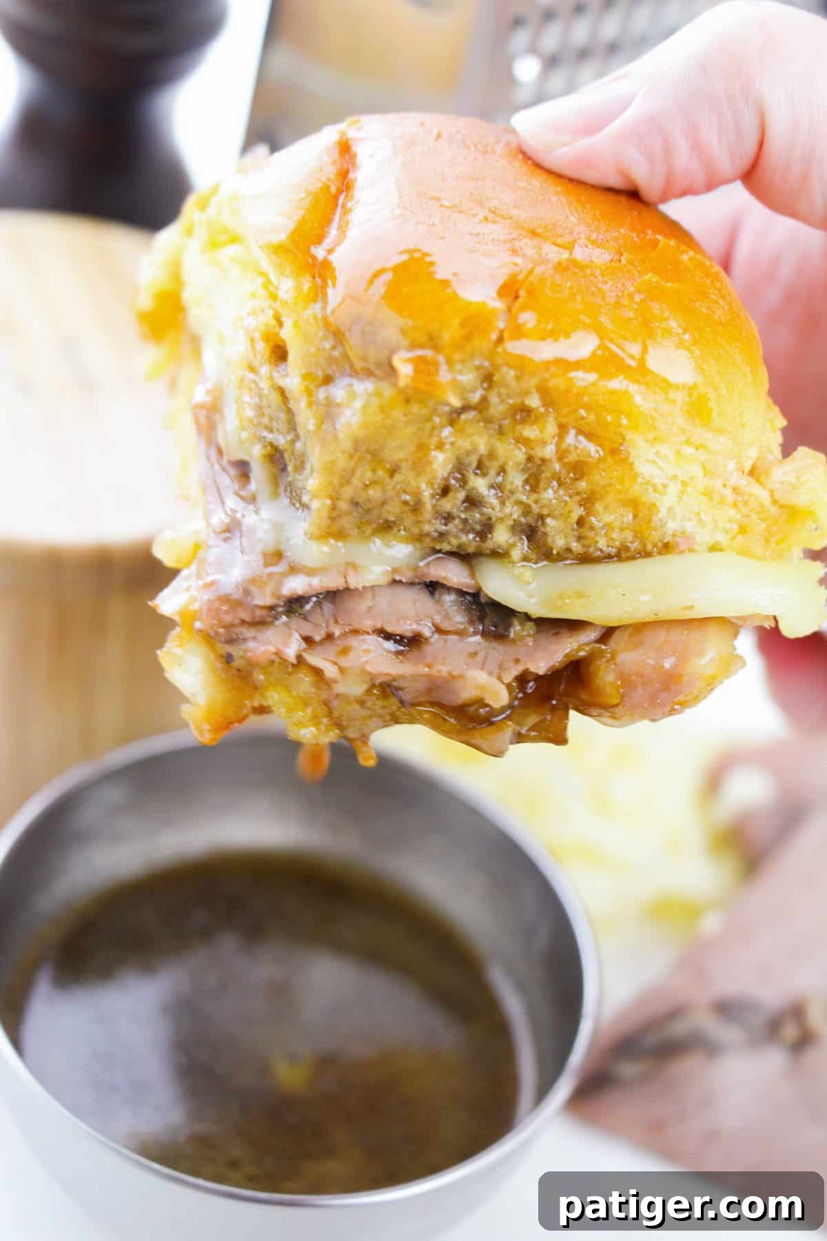 Hand holding French dip roast beef slider and dipping it in au jus sauce.