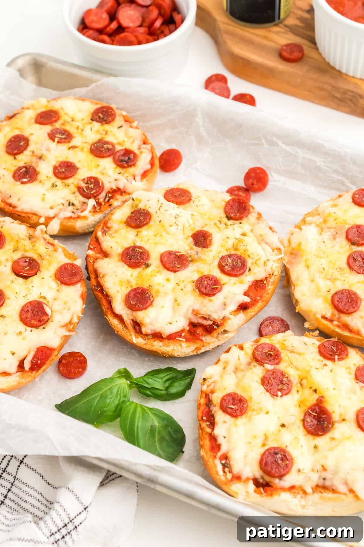 Air fryer bagel pizzas on white serving platter with fresh basil.