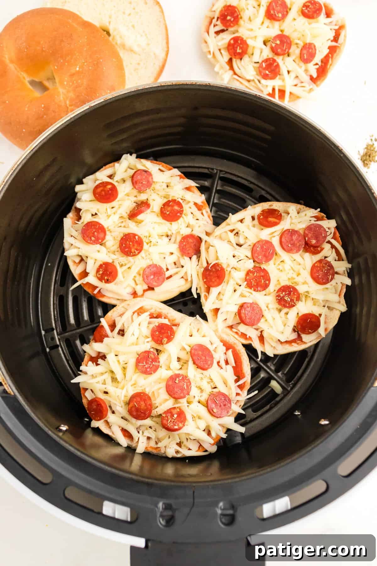 Three uncooked pizza bagels in the basket of an air fryer.