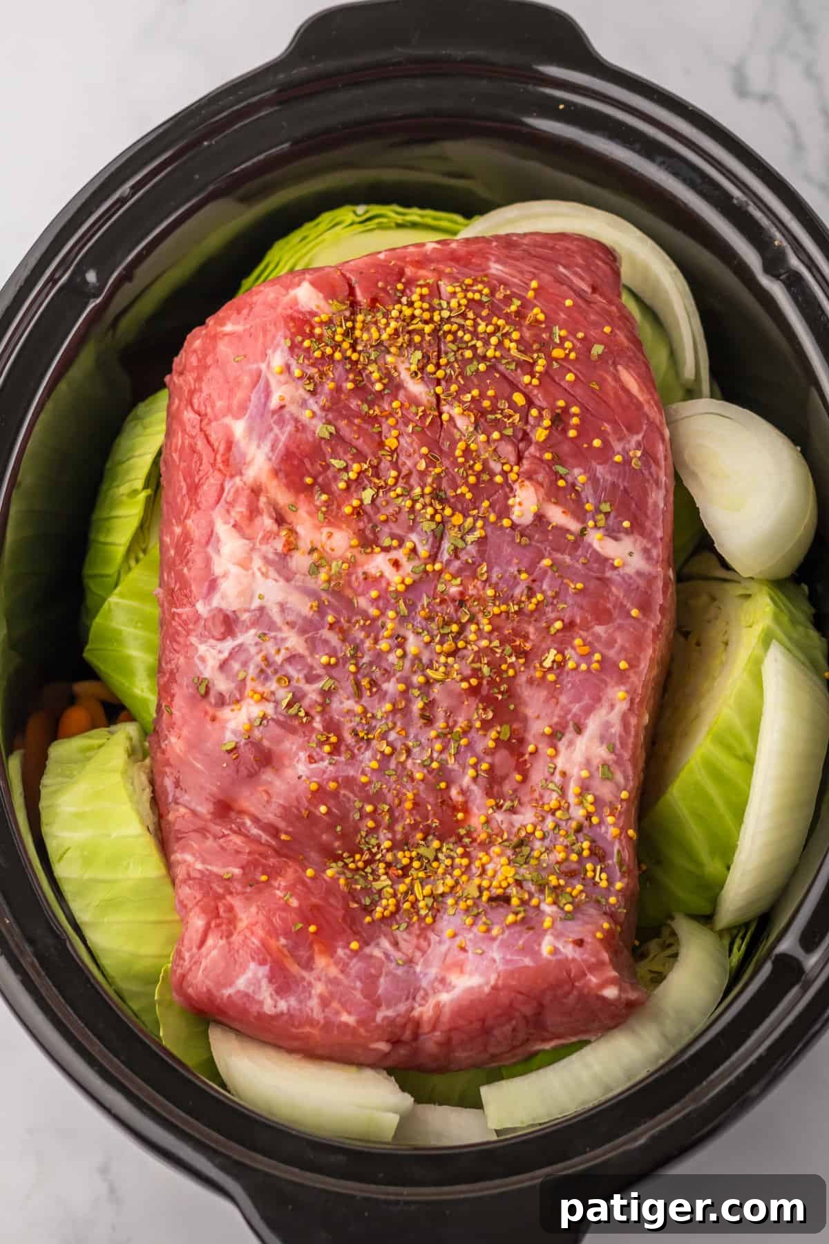 Melt-in-Your-Mouth Slow Cooker Corned Beef 4 Corned beef brisket surrounded by cabbage wedges, onions, and carrots layered in a slow cooker.