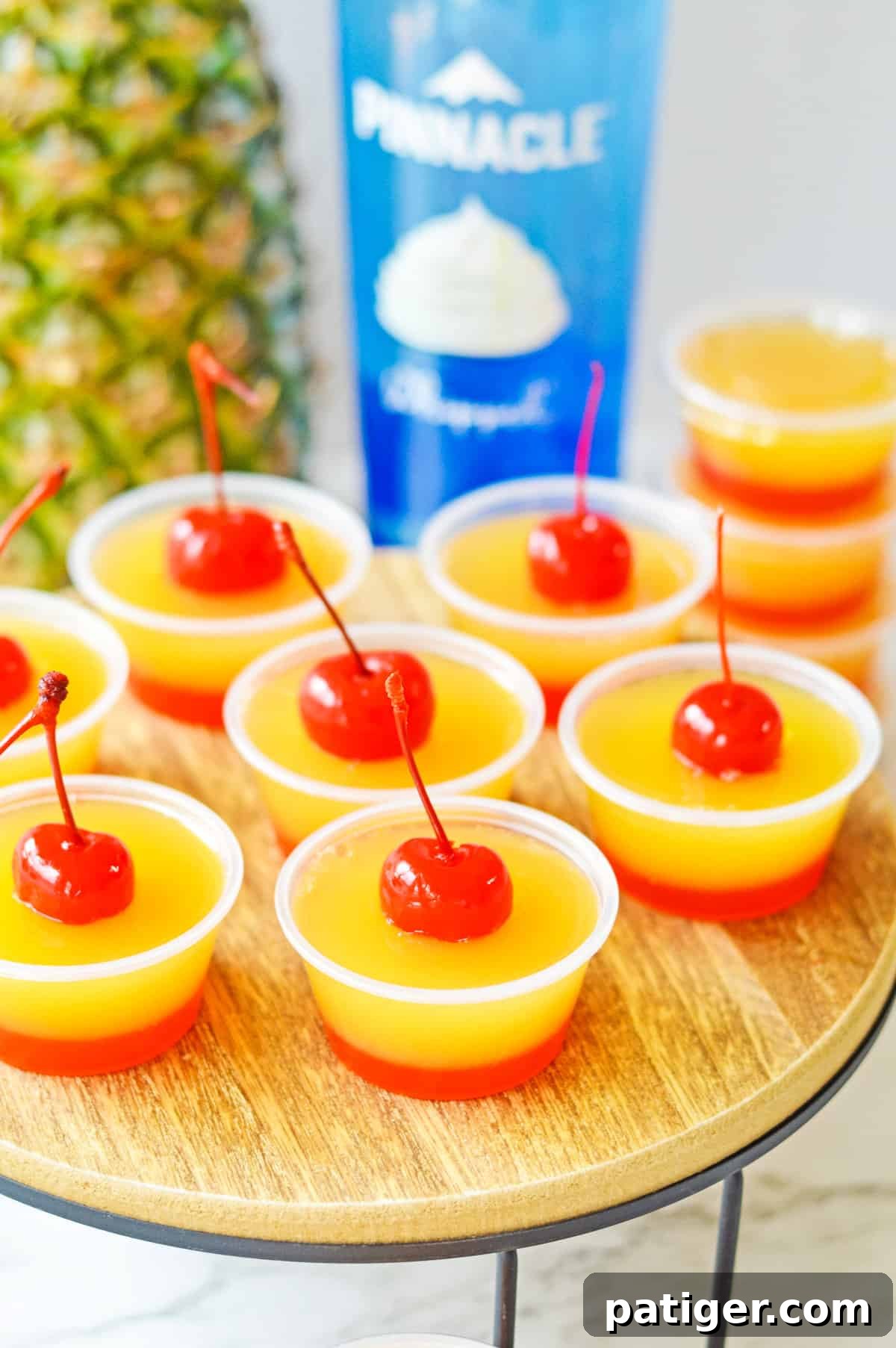 Caramel Pineapple Jell-O Shots 2 Pineapple upside-down cake jello shots with two distinct layers: a red cherry bottom layer and yellow pineapple top layer, and a cherry on top.