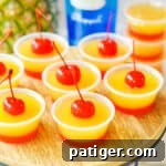 Caramel Pineapple Jell-O Shots 9 Pineapple upside down cake jello shots with two distinct layers: a red cherry bottom layer and yellow pineapple top layer, and a cherry on top.