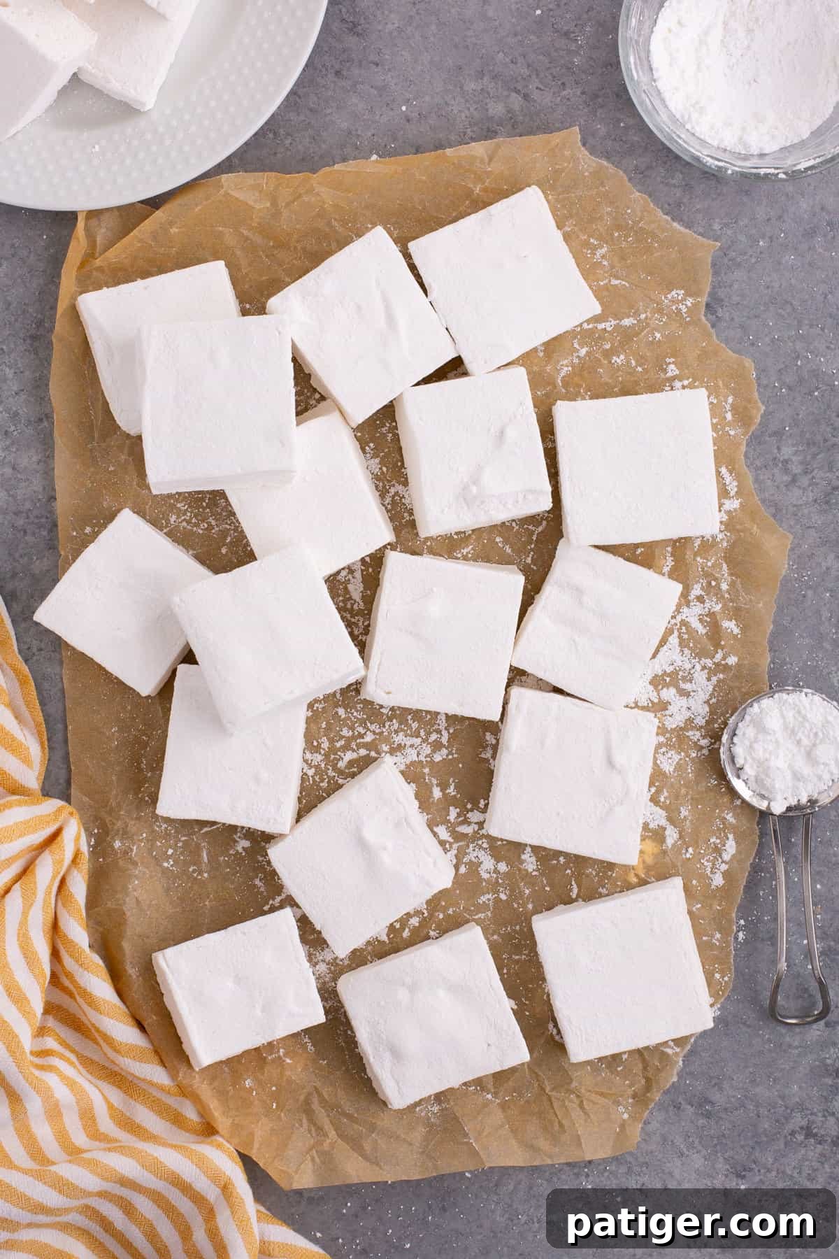 Homemade marshmallows on brown parchment paper with dusting of confectioners sugar.