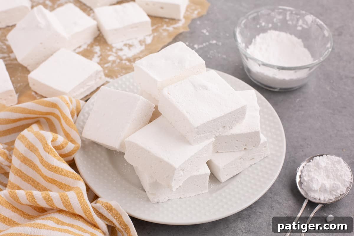 Fluffy homemade marshmallows piled on white plate coated in powdered sugar.