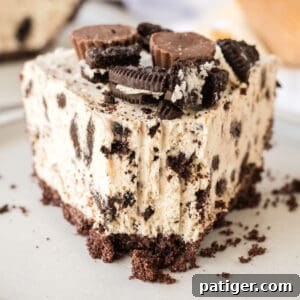 Decadent Oreo Peanut Butter Pie 11 Slice of Oreo Peanut Butter Pie with chocolate cookie crust, peanut butter filling with crushed Oreos, and Reese's and Oreos on top. A fork has taken a bite out of the pie.