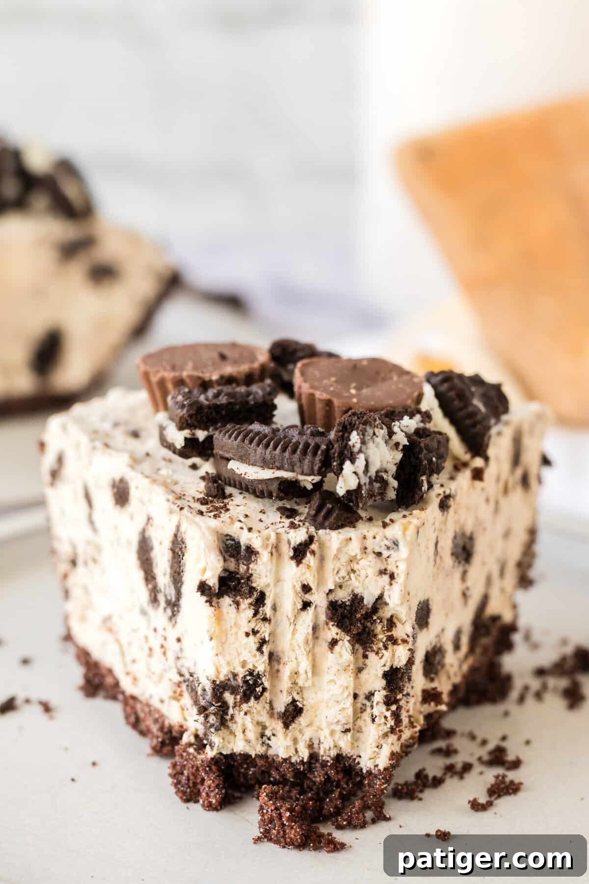 Decadent Oreo Peanut Butter Pie 3 A perfect slice of Oreo Peanut Butter Pie, showing the chocolate crust, creamy peanut butter filling with crushed Oreos, and garnished with mini Reese's cups and chopped Oreos. A fork has taken a bite out.