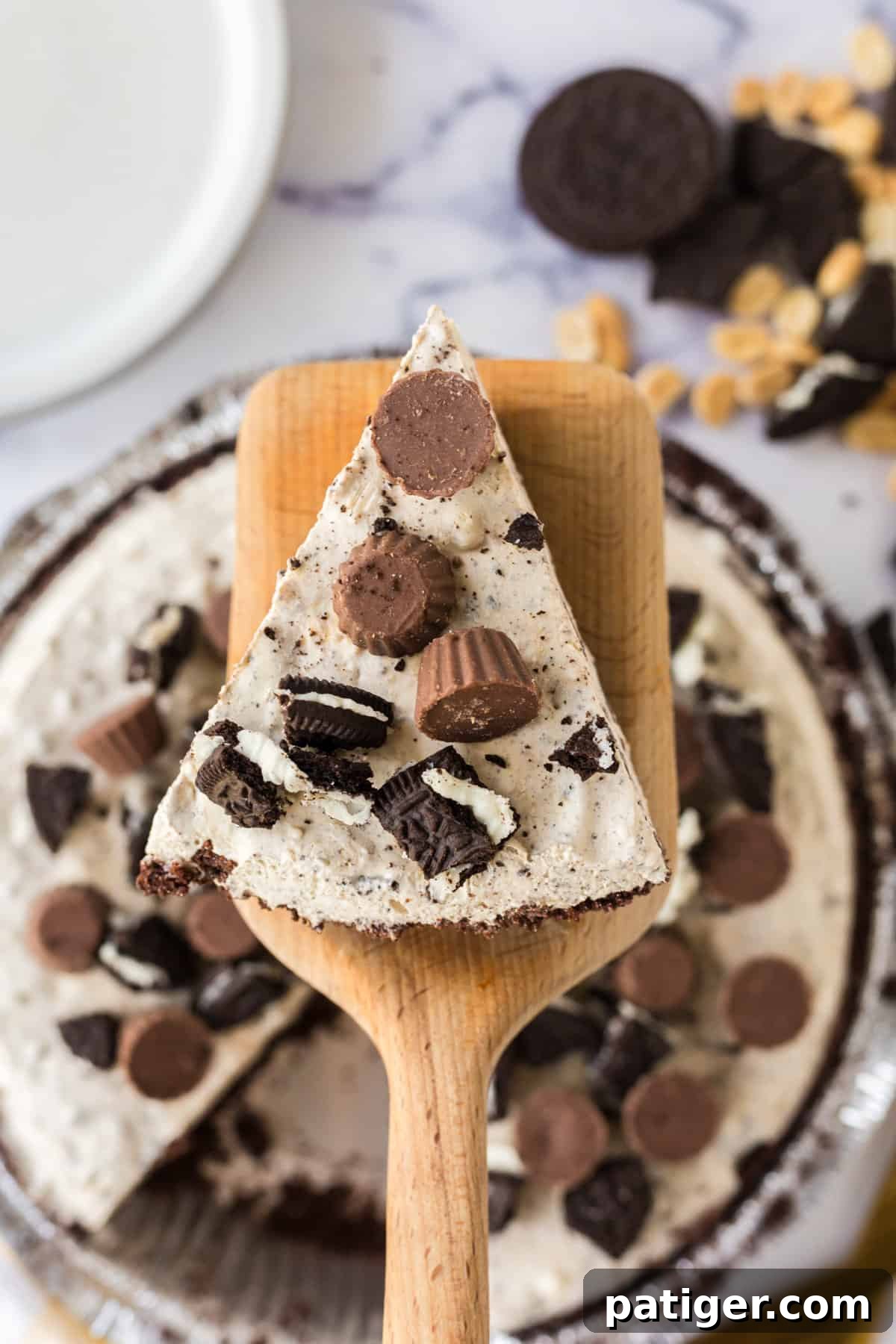 Decadent Oreo Peanut Butter Pie 8 A slice of Oreo peanut butter pie being gently lifted from the main pie with a wooden pie server, revealing the firm, creamy texture.