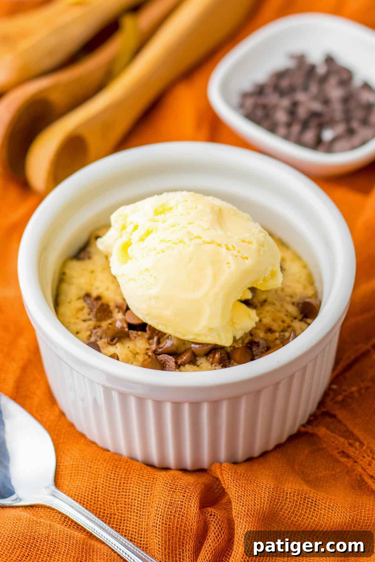 Microwave Chocolate Chip Cookie in a ramekin topped with vanilla ice cream, ready to be enjoyed with a spoon.