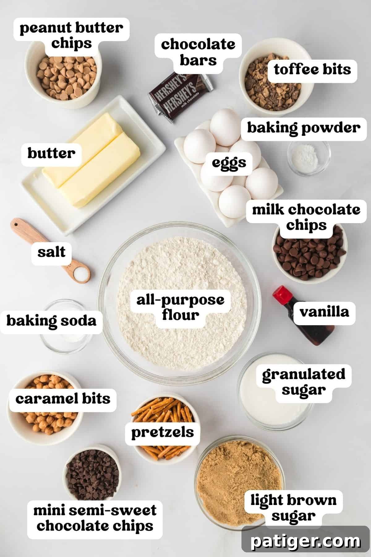 Mega Mix Cookies 4 Kitchen sink cookie ingredients on countertop: peanut butter chips, chocolate bars, toffee bits, two sticks of butter, eggs, baking powder, salt, flour, milk chocolate chips, vanilla, baking soda, pretzels, granulates sugar, light brown sugar, caramel bits, and mini semi-sweet chocolate chips.