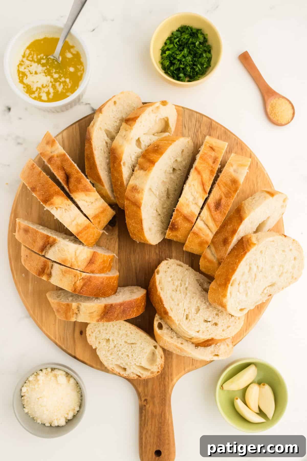 Golden Garlic Bread in Minutes 4 Sliced bread on a cutting board, surrounded by melted butter, Parmesan cheese, garlic cloves, garlic powder, and chopped parsley, ready for making garlic bread.