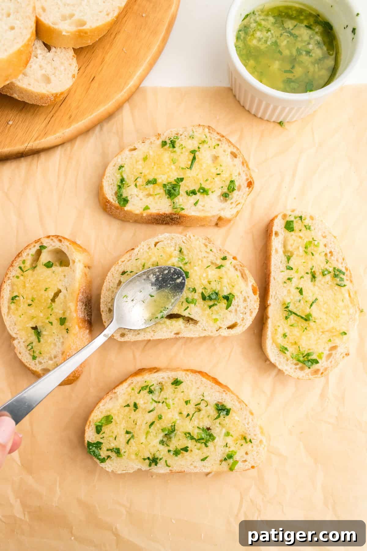 Golden Garlic Bread in Minutes 6 Slices of garlic bread laid on parchment paper with the butter mixture being spooned onto them, preparing for air frying.
