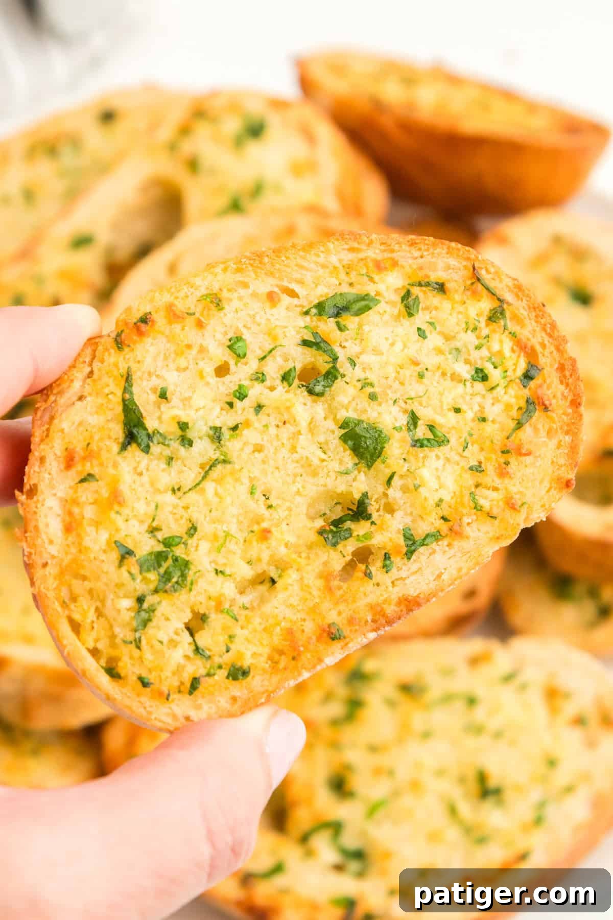 Golden Garlic Bread in Minutes 10 A hand holding a piece of thick, crispy air fryer garlic bread garnished with fresh parsley.