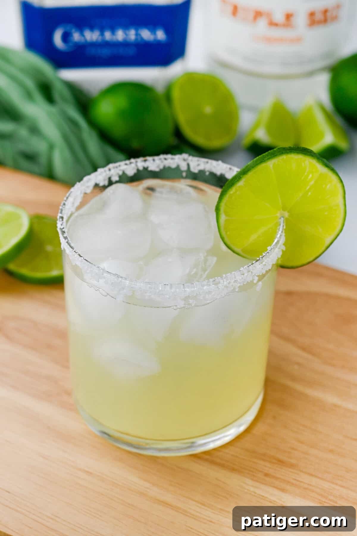 A vibrant classic margarita on the rocks, complete with a lime garnish and salted rim, with bottles of spirits and fresh limes artfully blurred in the background.