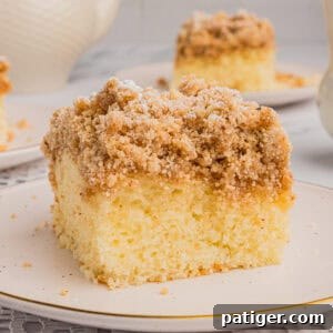 Slice of New York style crumb cake with thick layer of crumb topping. Another slice and a teapot are in the background.