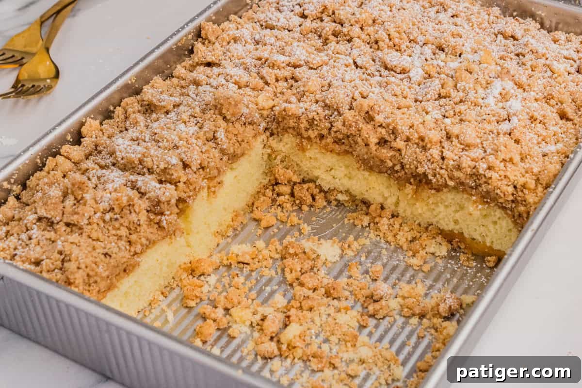 A shortcut New York style crumb cake, freshly baked in a metal baking pan, with several squares already removed, showcasing its delicious layers.