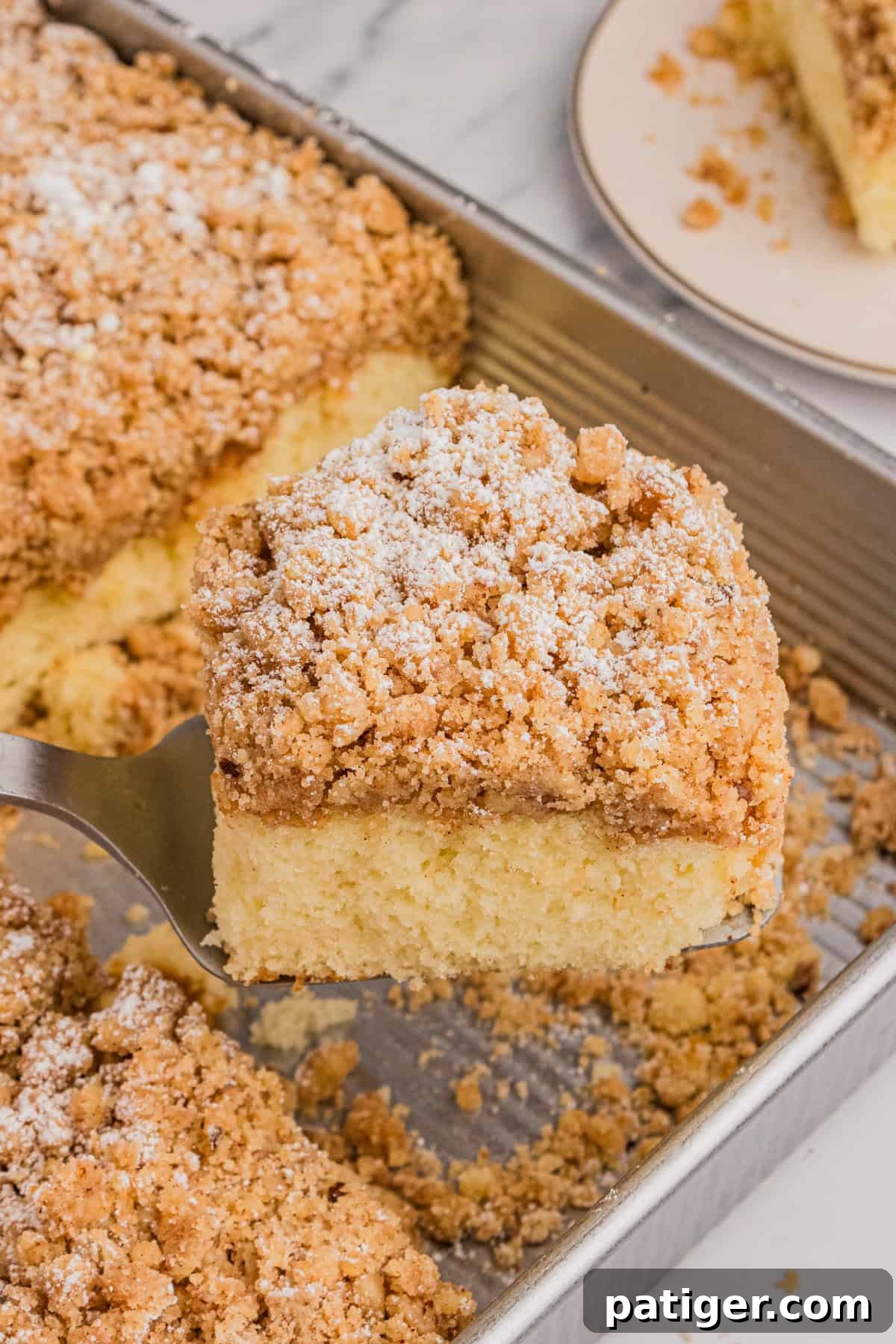 A slice of cake mix crumb cake being carefully lifted from the baking pan using a metal spatula, highlighting its thick crumb topping and moist cake layer.