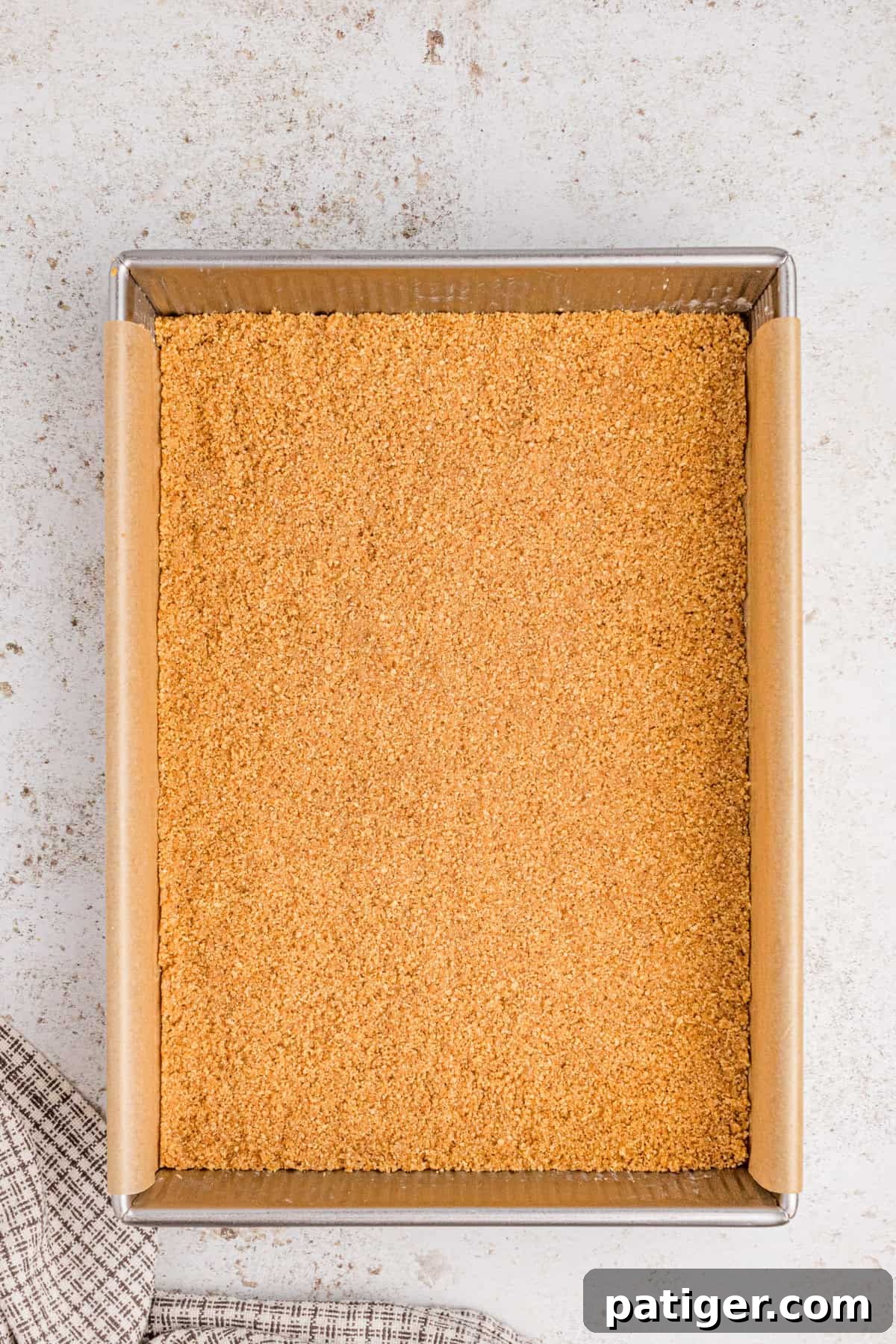 Graham cracker crust pressed evenly into the bottom of a lined baking pan.