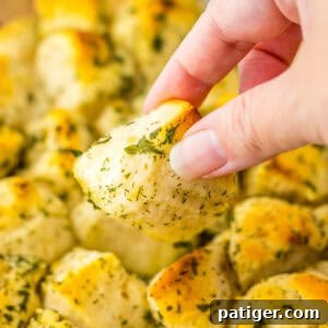 Piece of pull apart herb biscuits being taken from baking dish.