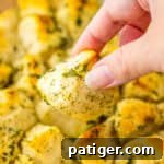 Piece of pull apart herb biscuits being taken from baking dish.