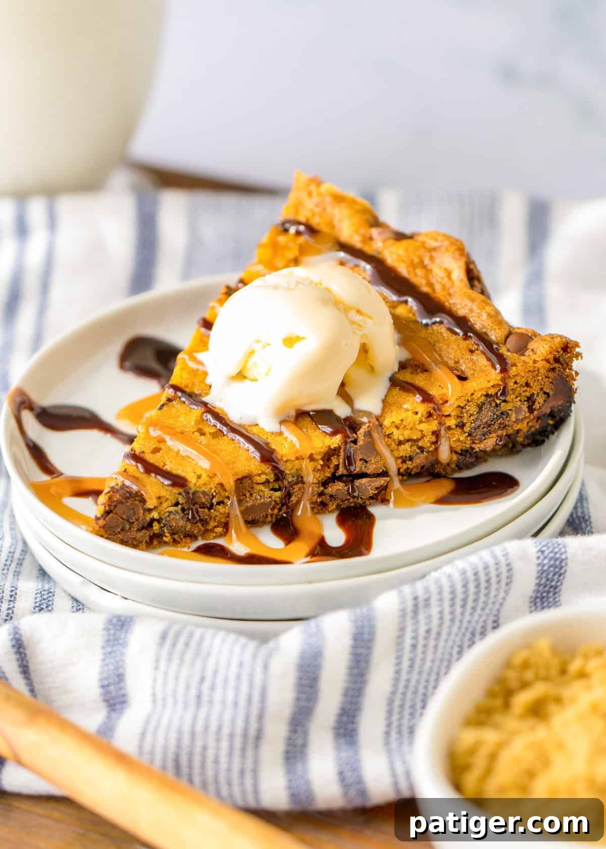 Ultimate Slow Cooker Chocolate Chip Cookie 2 A large, triangular slice of slow cooker chocolate chip cookie served warm with a scoop of melting vanilla ice cream, topped with rich chocolate and sweet caramel syrup. The cookie is thick and golden-brown with visible chocolate chips.