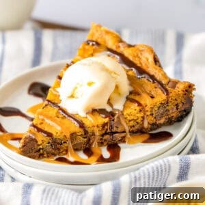 Slow Cooker Chocolate Chip Cookie cut into triangular piece and served with a scoop of vanilla ice cream, chocolate syrup, and caramel syrup.