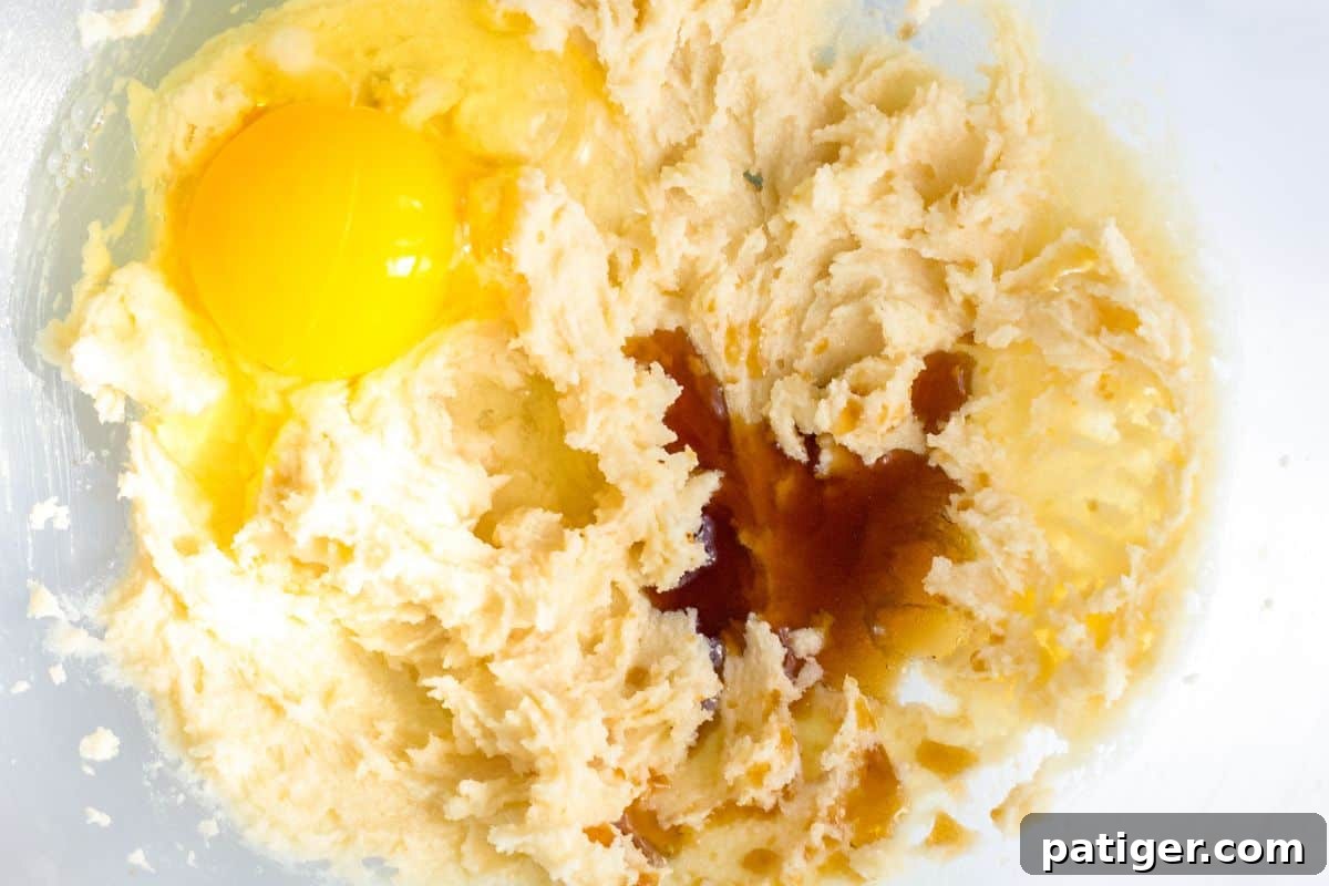 Ultimate Slow Cooker Chocolate Chip Cookie 5 A mixing bowl with creamed butter and sugar, now with a large egg and pure vanilla extract added, signifying the next step in preparing the cookie dough.