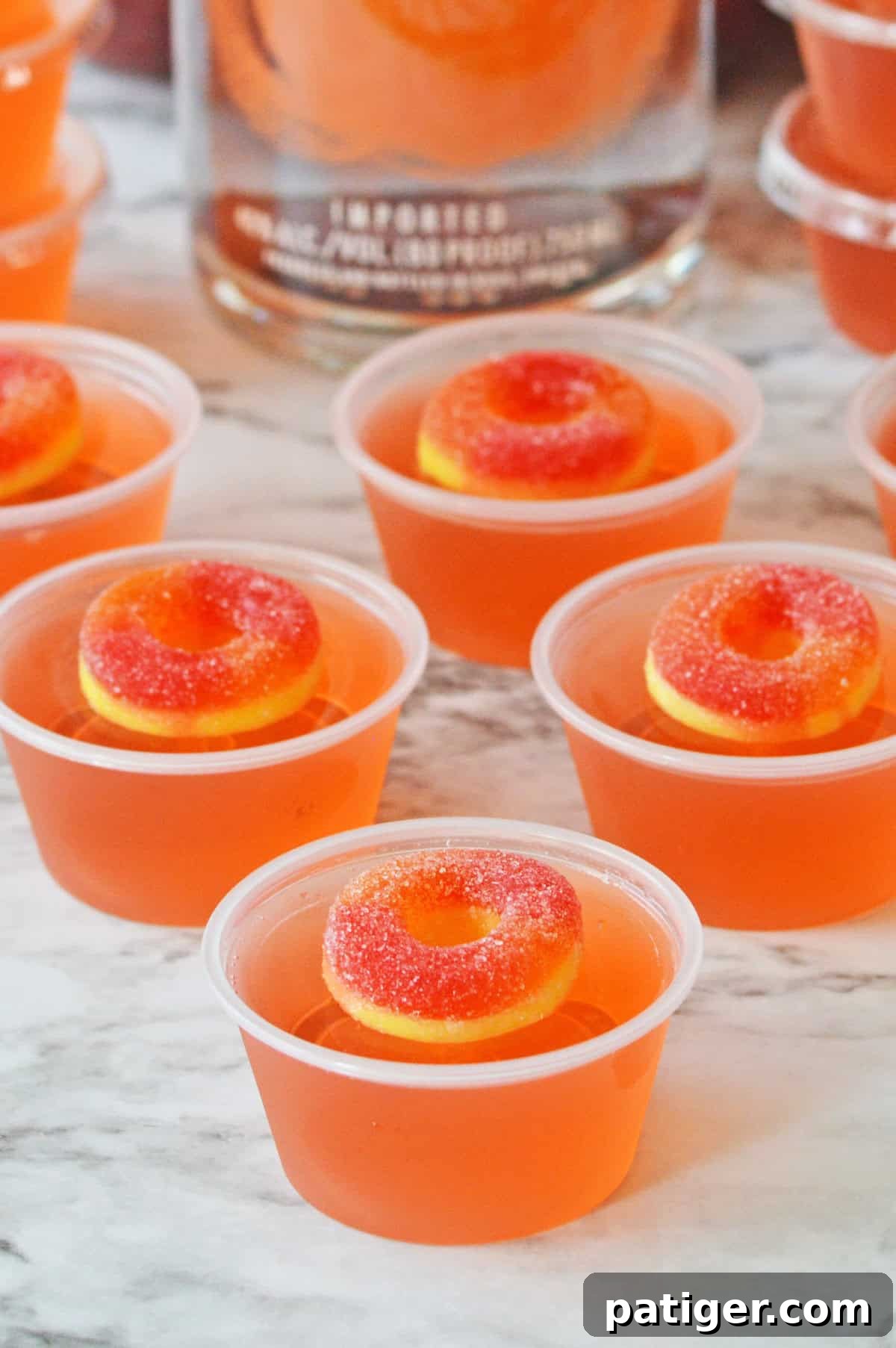 Peach vodka jello shots with peach ring candy on top and bottle of peach vodka in the background.