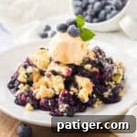 A small image of 4-ingredient blueberry cobbler served on a white plate with a scoop of ice cream.