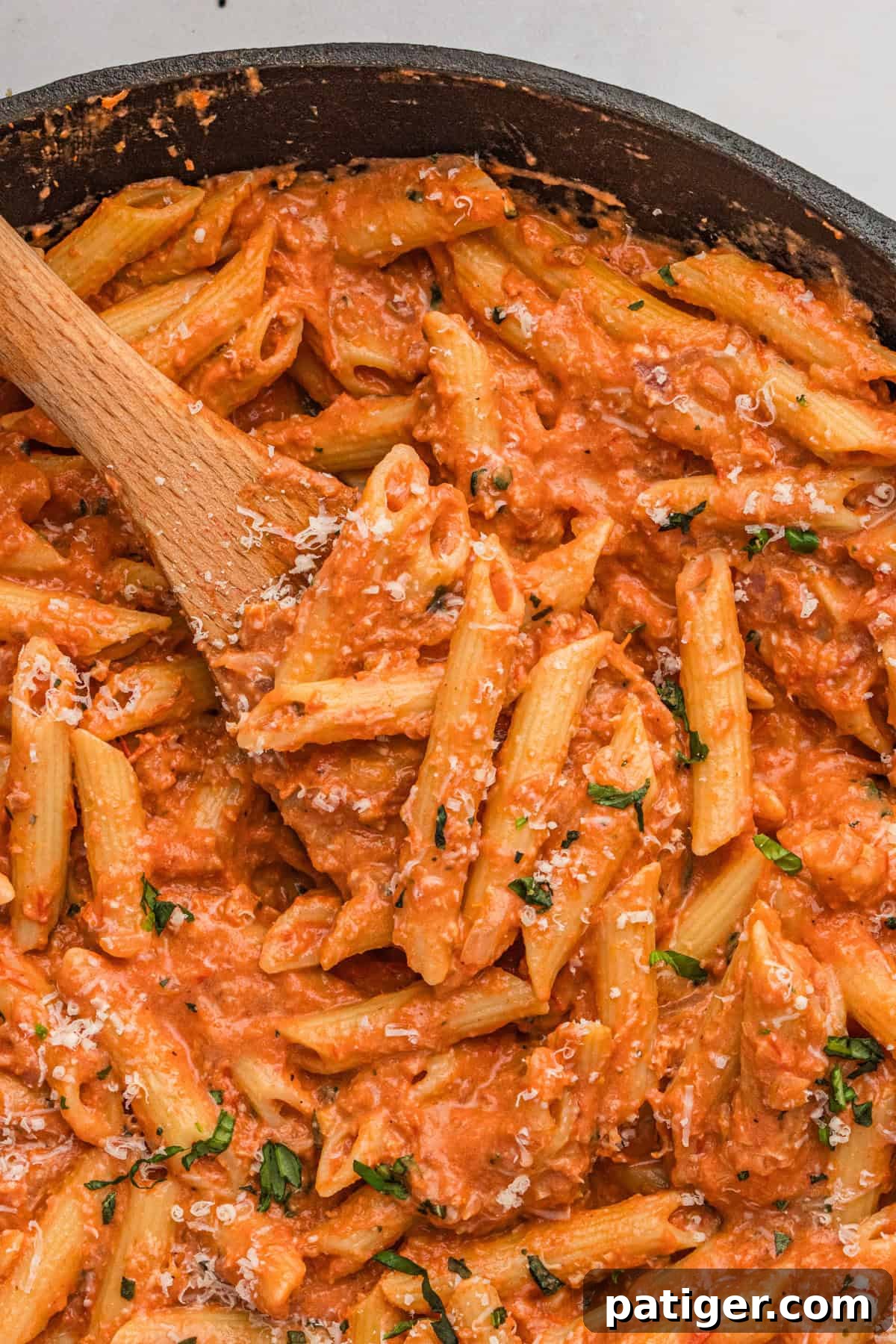 Creamy penne alla vodka in large skillet with wooden spoon, garnished with fresh basil.