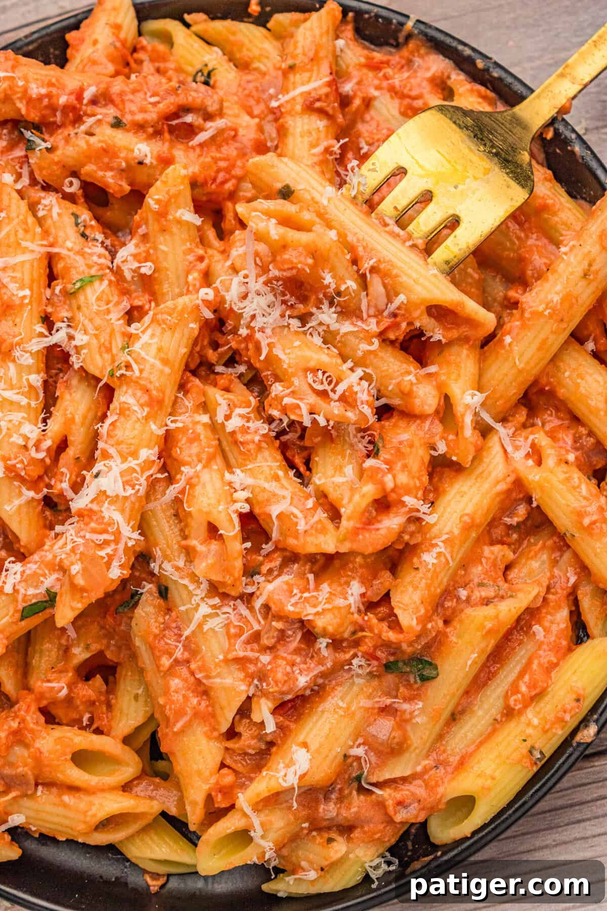 Penne with vodka sauce served in a white bowl, generously topped with grated Parmesan and fresh basil leaves.