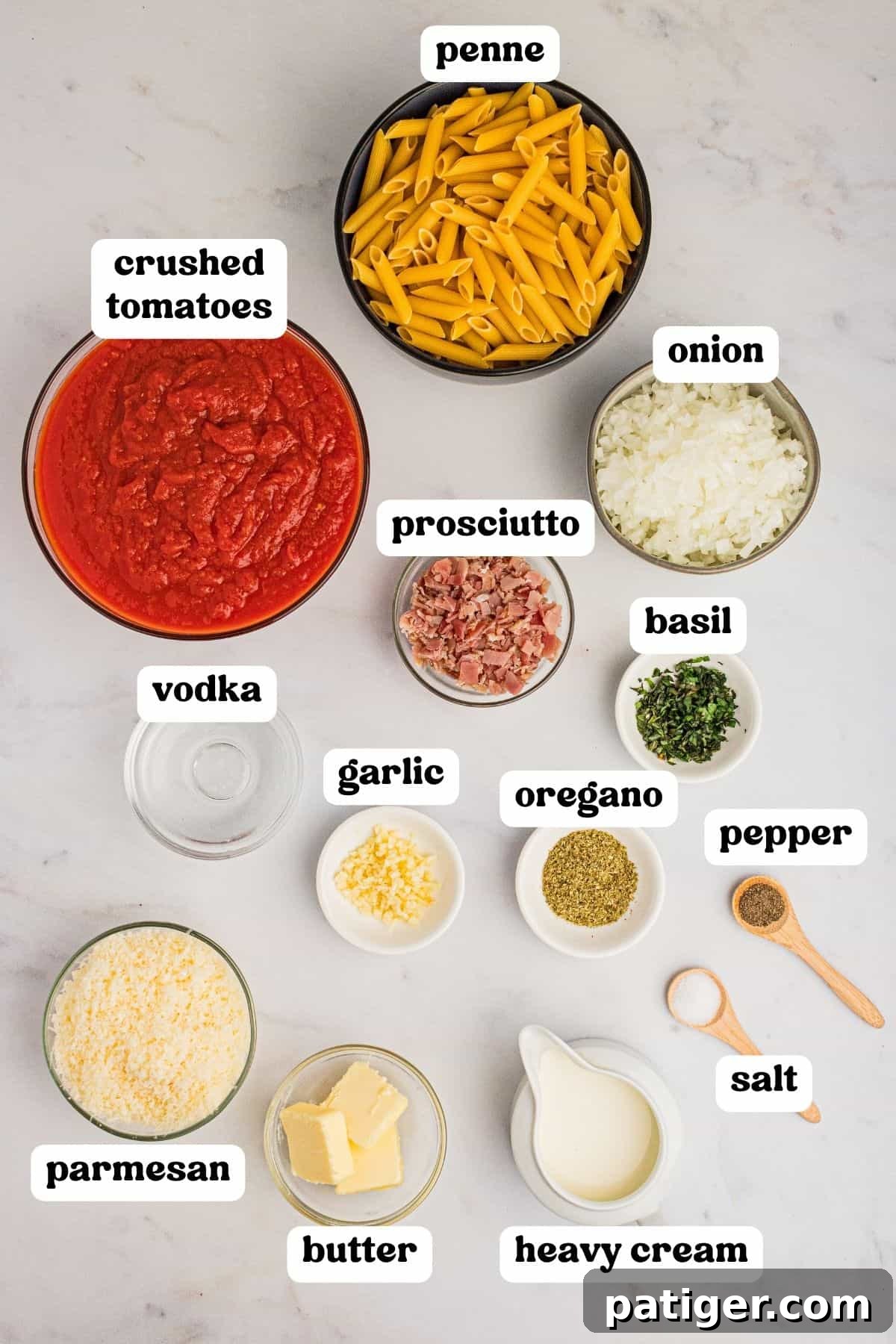 A flat lay of fresh ingredients for penne with vodka sauce, including penne pasta, tomatoes, heavy cream, parmesan, vodka, and herbs.