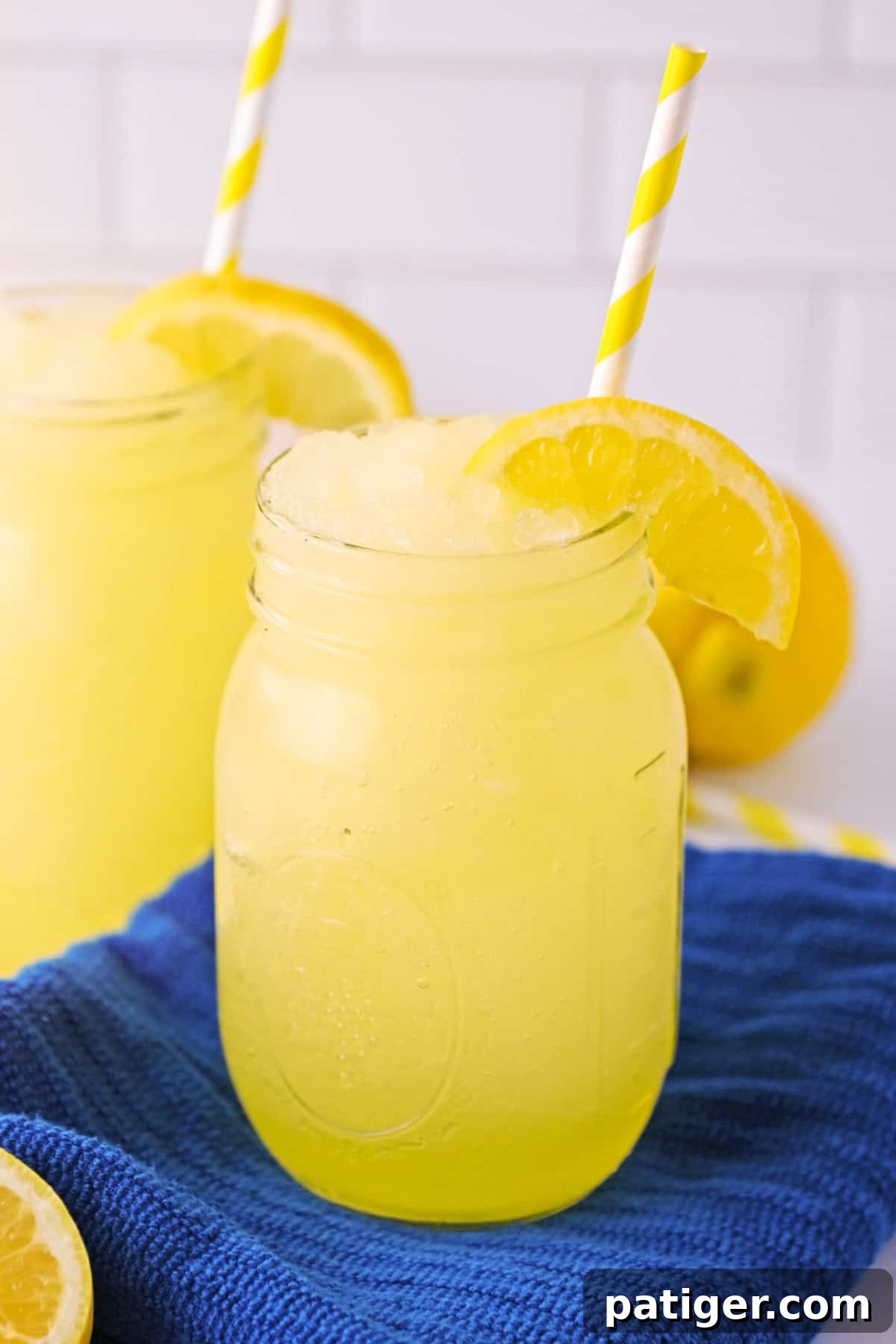 Frozen lemonade slushies garnished with slice of lemon and served in mason jars with straws.