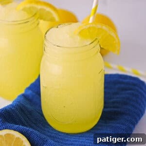 Frozen lemonade slushies garnished with slice of lemon and served in mason jars with yellow striped straws.