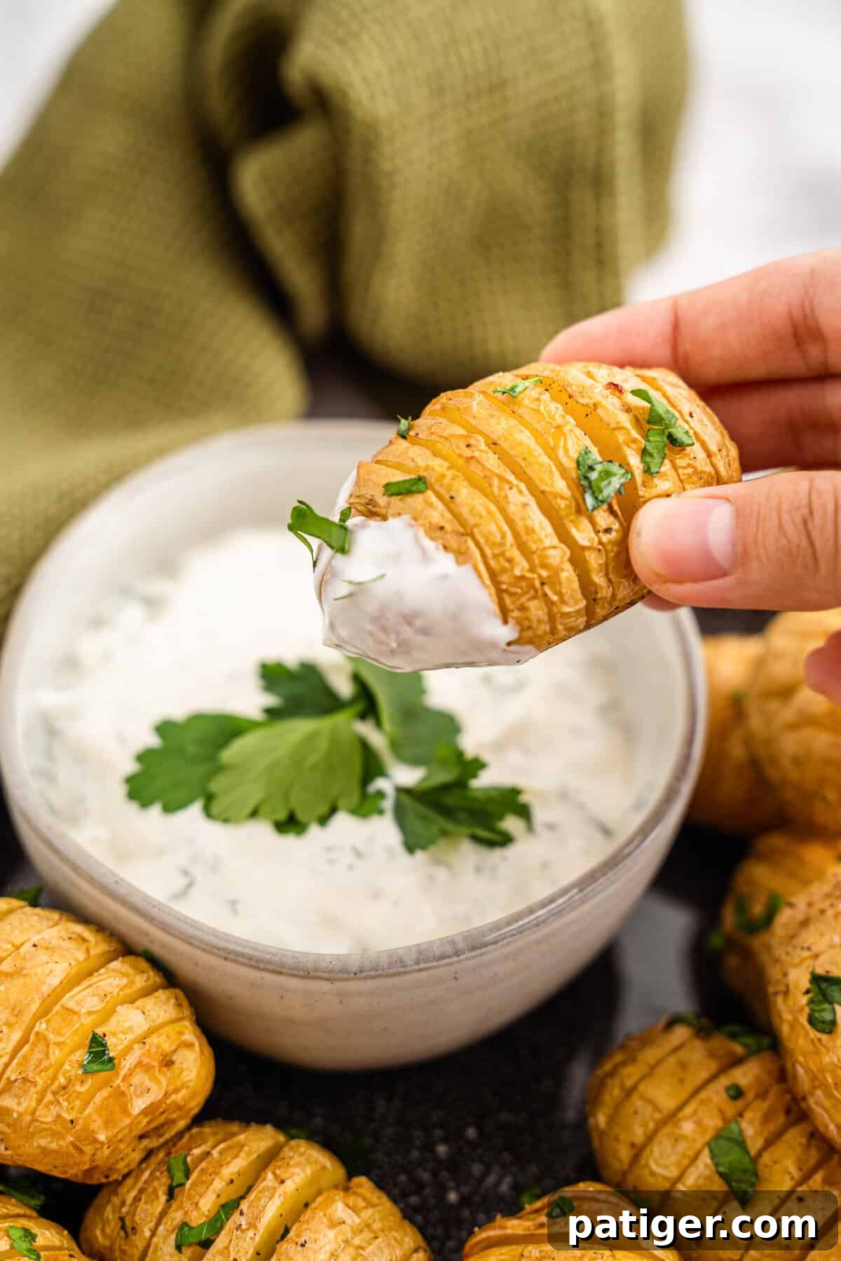 A golden, crispy Mini Hasselback Potato being dipped into a bowl of creamy, green homemade dill dip.