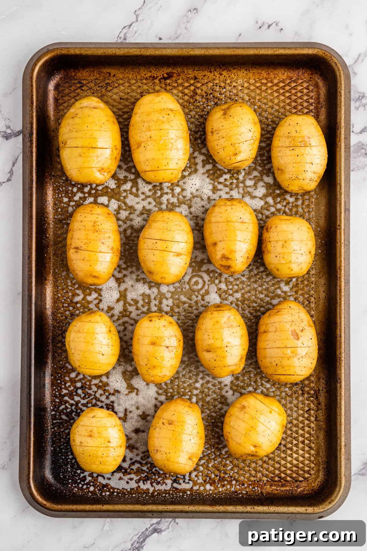 Mini potatoes on a baking sheet, sliced in the hasselback style and seasoned generously with salt and pepper, ready for roasting.