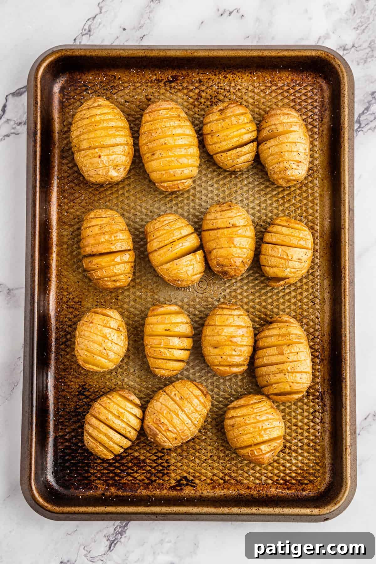 A baking sheet filled with perfectly golden-brown and crispy seasoned mini hasselback potatoes, fresh out of the oven.