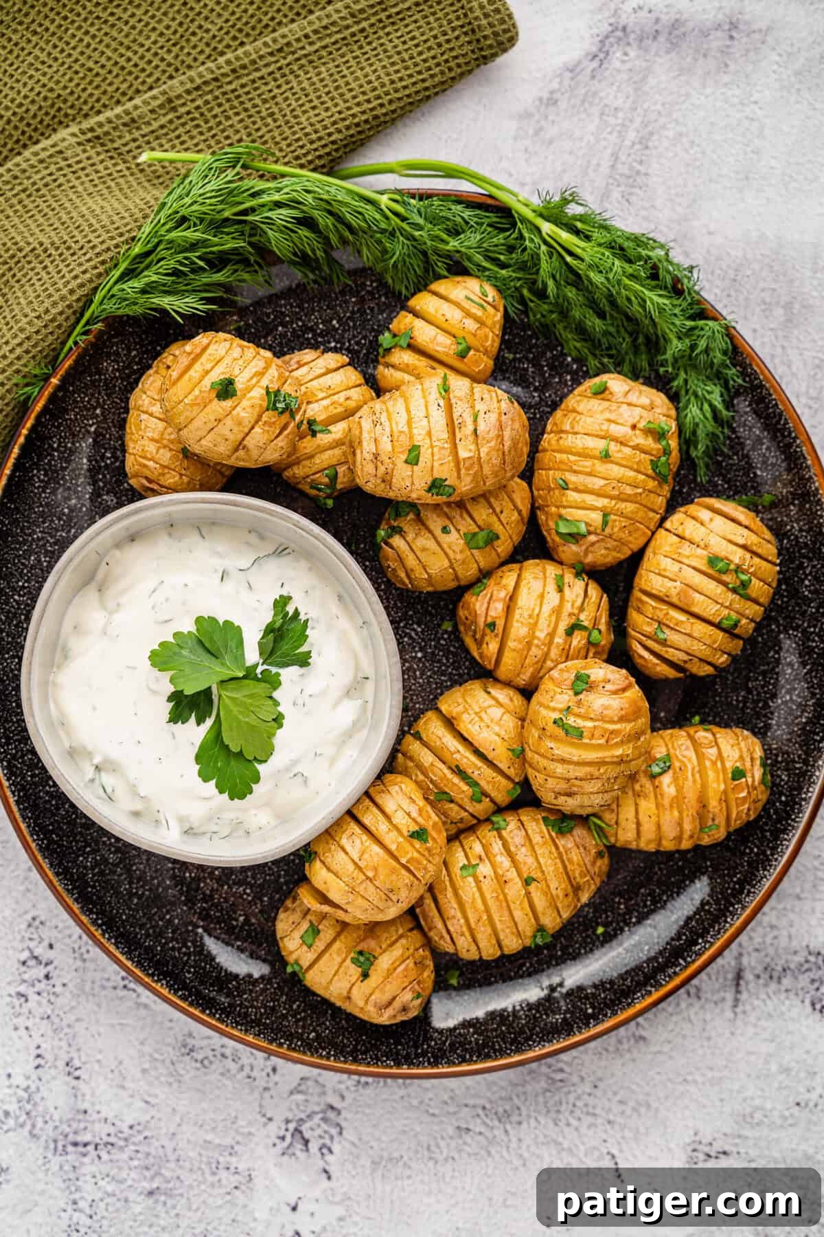 A beautifully presented plate of hot, crispy Mini Hasselback Potatoes, garnished with fresh herbs, alongside a bowl of creamy homemade dill dip.