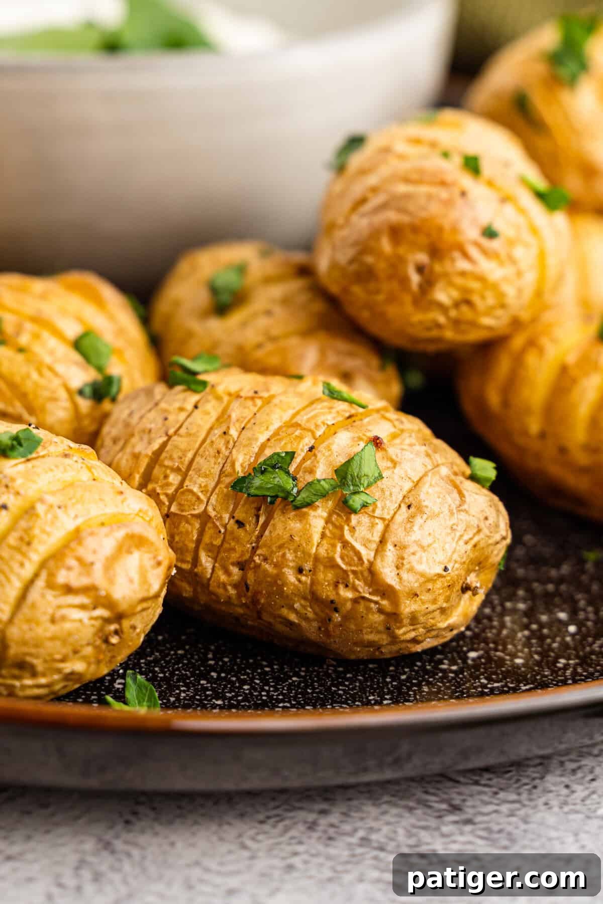 Close-up of perfectly crispy mini hasselback baked potatoes with numerous thin, fanned-out slices, showing off their golden-brown edges.
