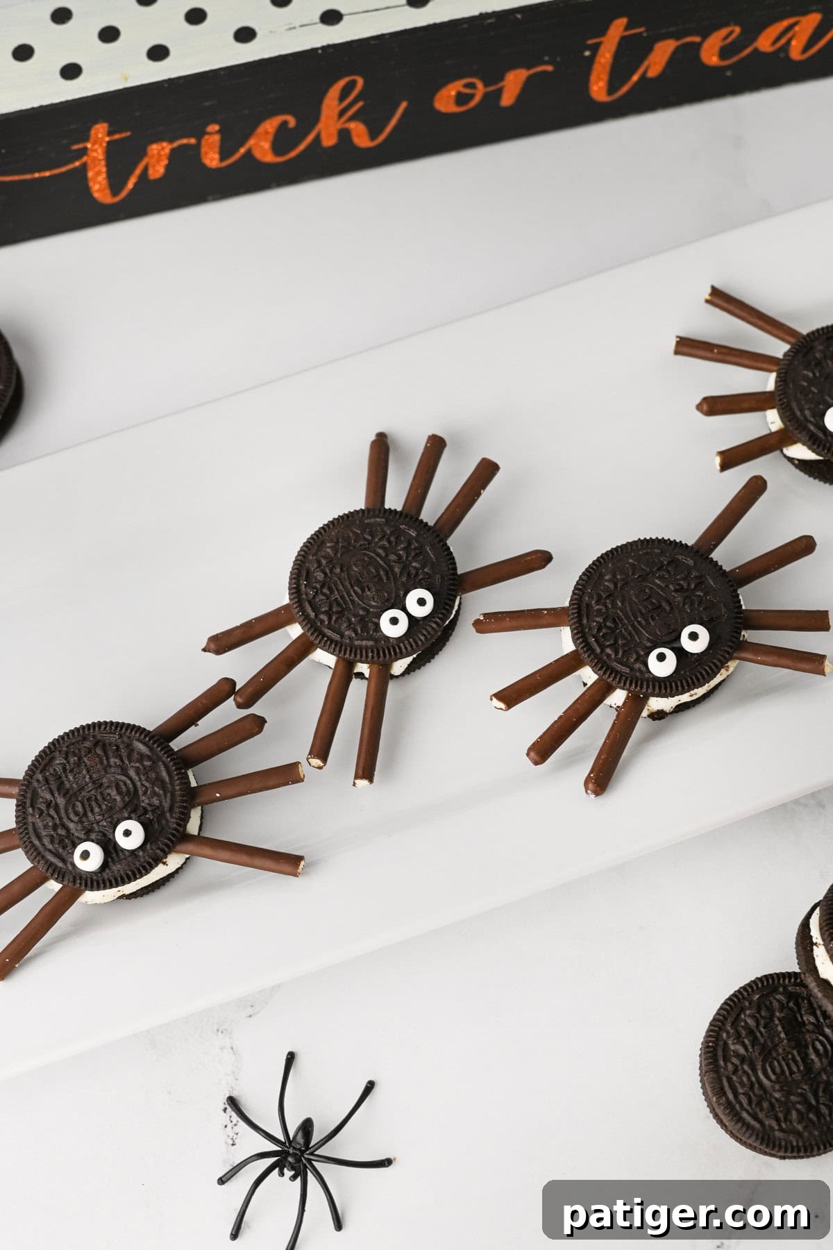 Oreo cookie spiders for Halloween served on white platter with halloween decor around them.