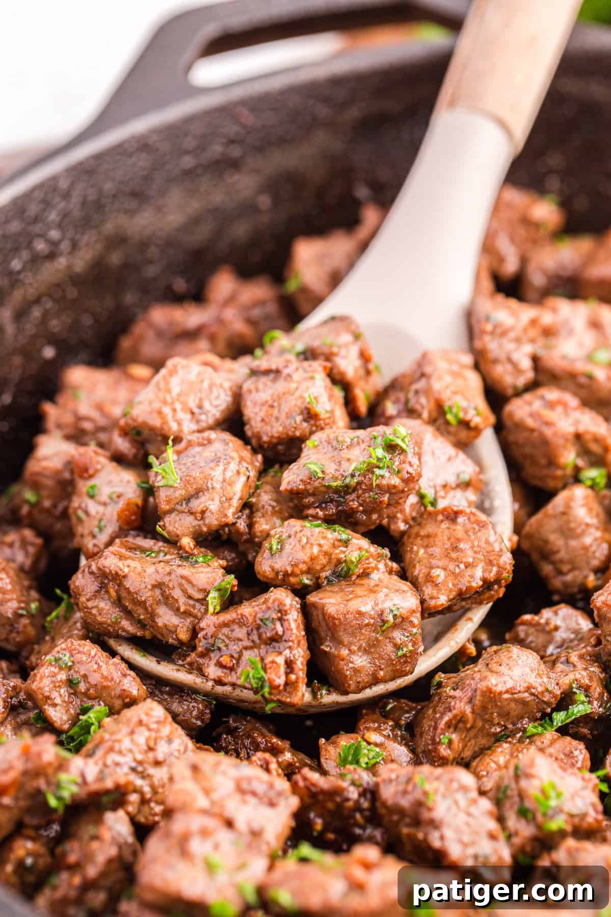 Golden Garlic Steak Bites 9 Spoon lifting tender garlic butter steak bites out of a skillet, coated in butter sauce.
