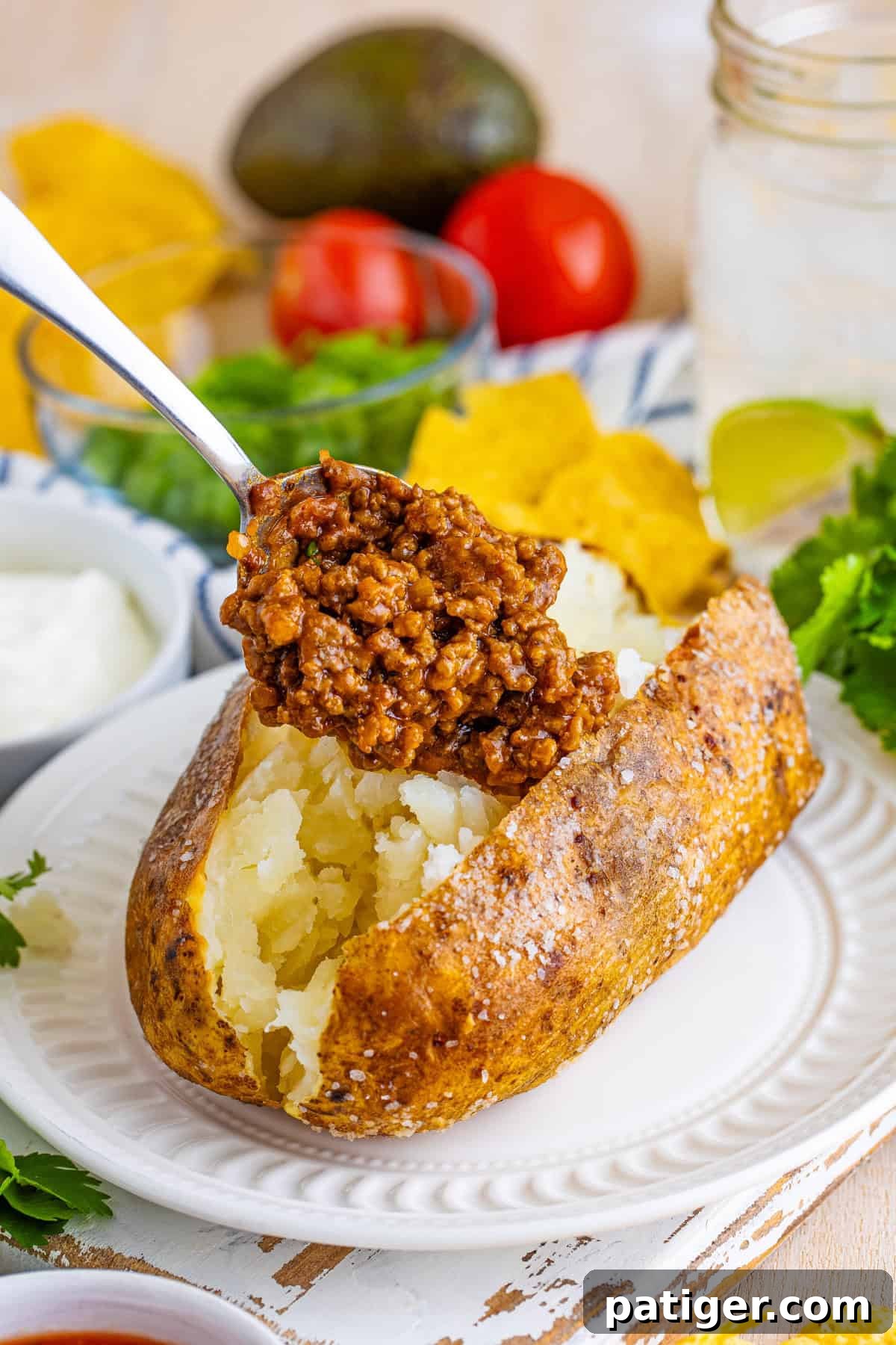 Taco Spud Boats 7 A baked potato with crispy salted skin sliced open, with a spoon scooping taco-seasoned ground beef into the fluffy center.