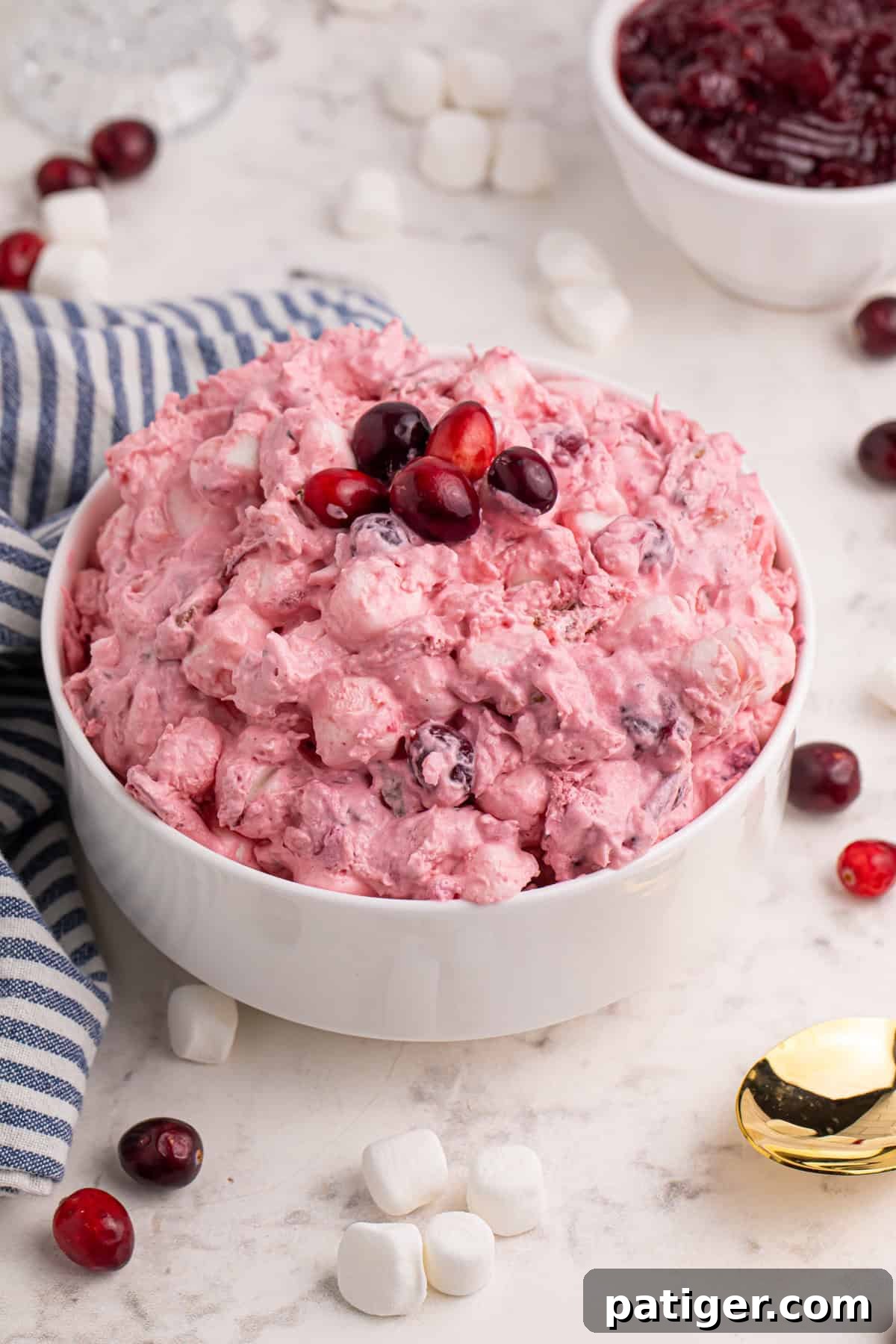 Bowl of cranberry fluff salad surrounded by marshmallows and cranberries.